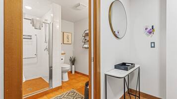 Une salle de bain moderne avec une douche à parois de verre, des carreaux blancs, des toilettes et une petite table avec un miroir.