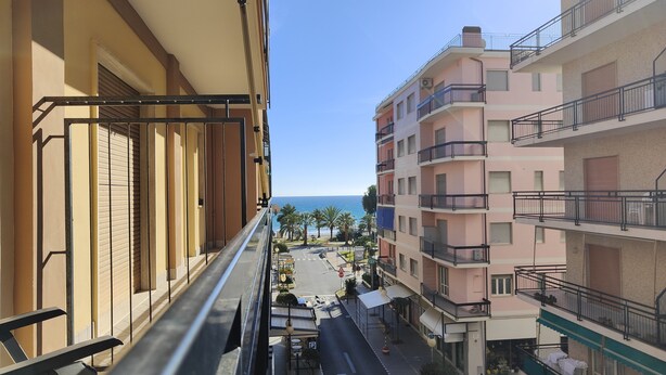 Een balkon met uitzicht op een straat met gebouwen, een heldere lucht en zee.
