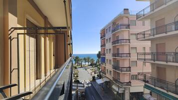 Ein Balkon mit Blick auf eine Straße, Gebäude, einem klaren Himmel und den Blick auf das Meer.