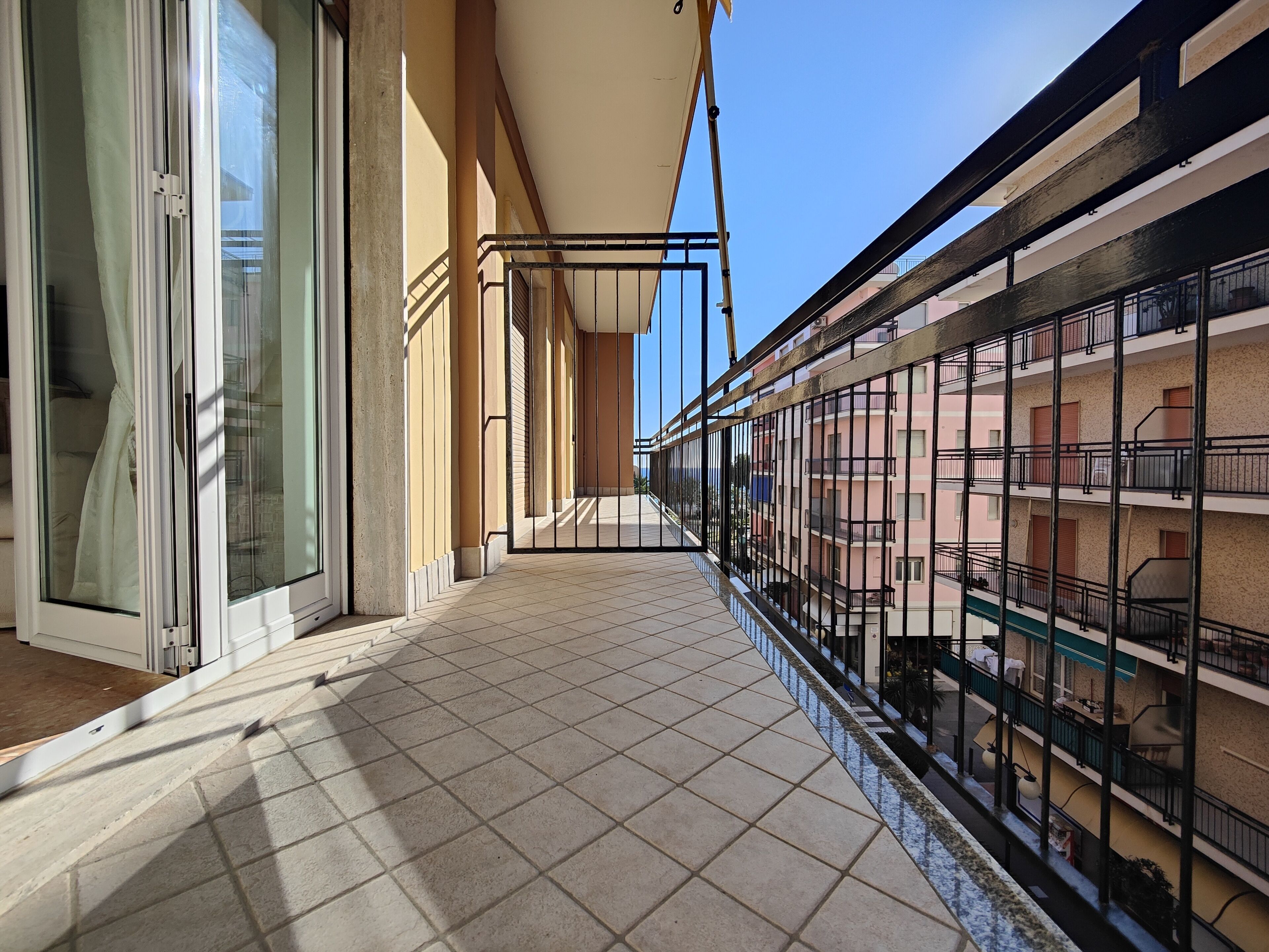 Ein Balkon mit Fliesenboden, einer Glastür und einem Metallgeländer.