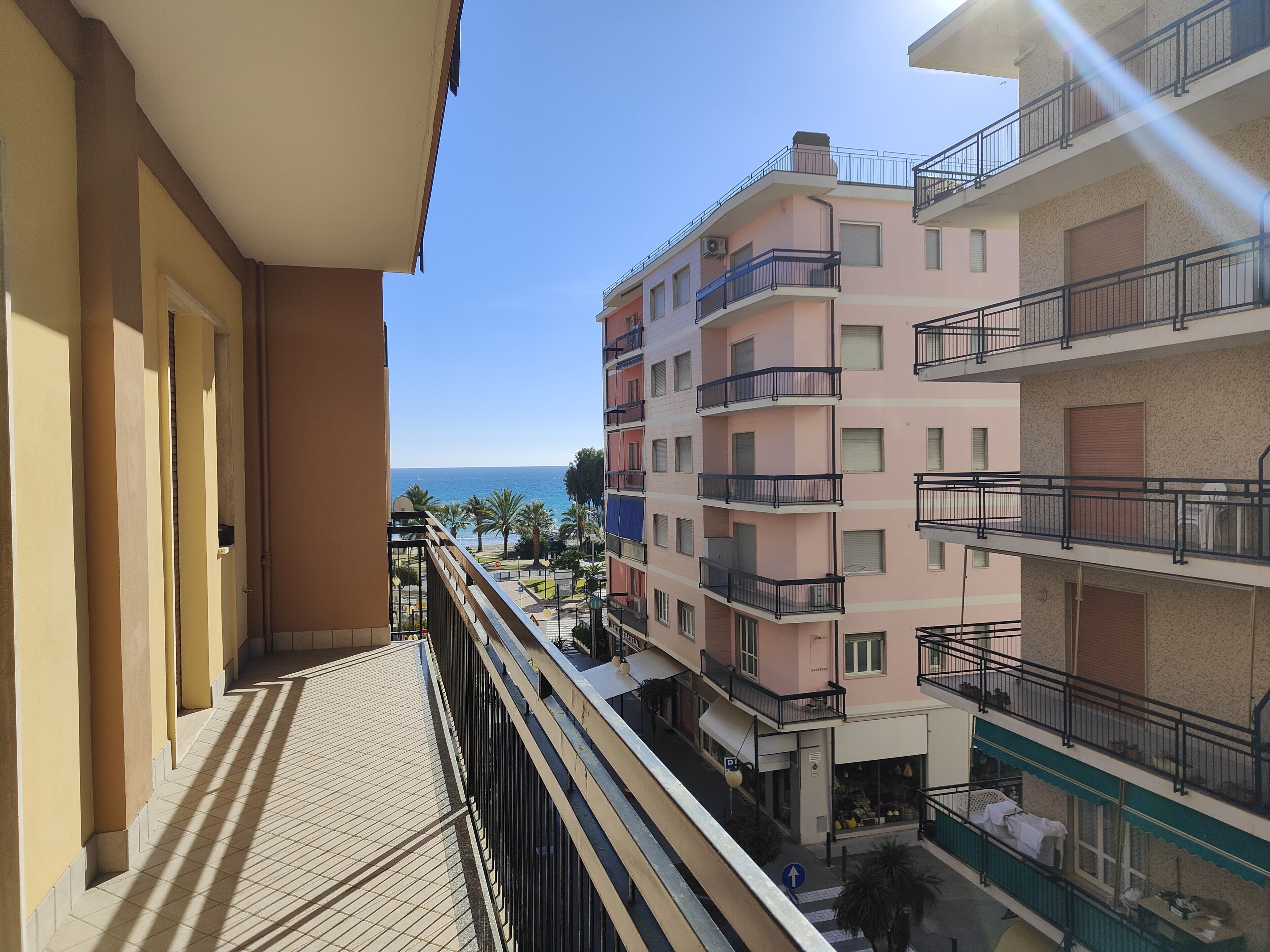 Un edificio de varios pisos con balcones, vista despejada al mar y un paseo de baldosas.