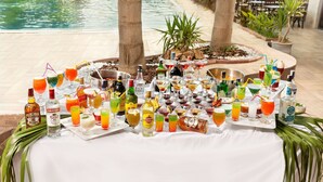 A table set with various cocktails and bottles of liquor, surrounded by palm trees and a pool in the background. - Dedeman Kemer Resort - Ultra All Inclusive (Kemer)
