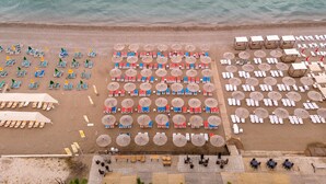 An aerial view of a beachside resort with rows of sun loungers and umbrellas, a pool area, and palm trees. - Dedeman Kemer Resort - Ultra All Inclusive (Kemer)