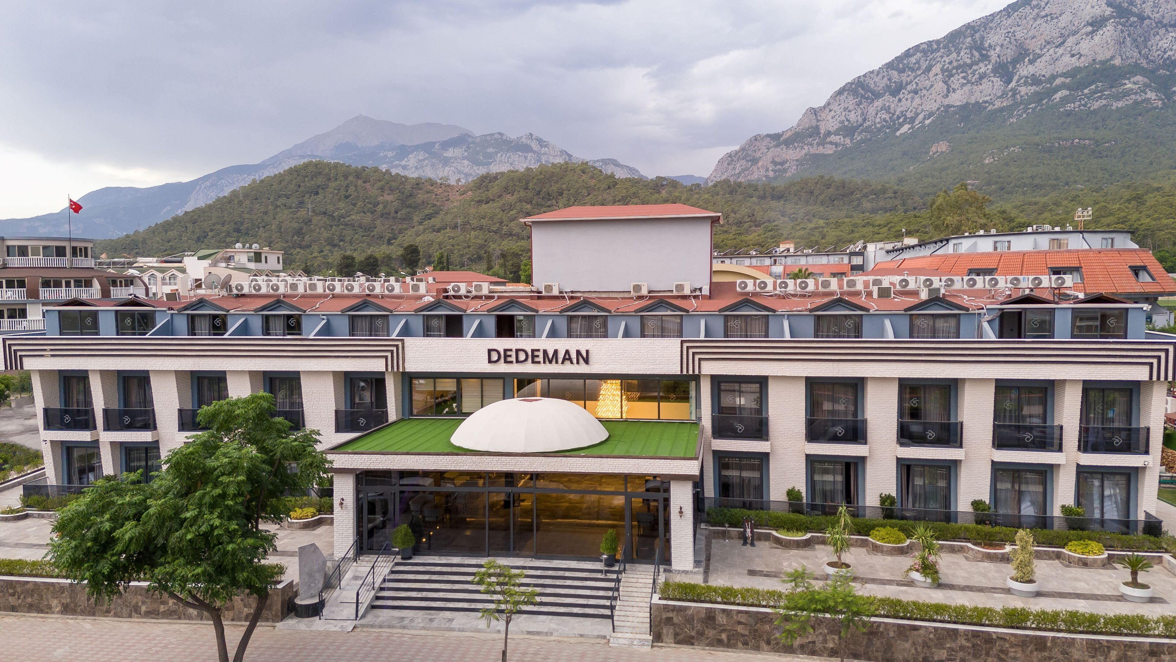 Un hotel con fachada moderna, techo verde y vistas a montañas al fondo.