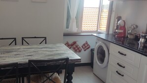 Een keuken met een houten tafel, stoelen, een wasmachine en een koffiezetapparaat.