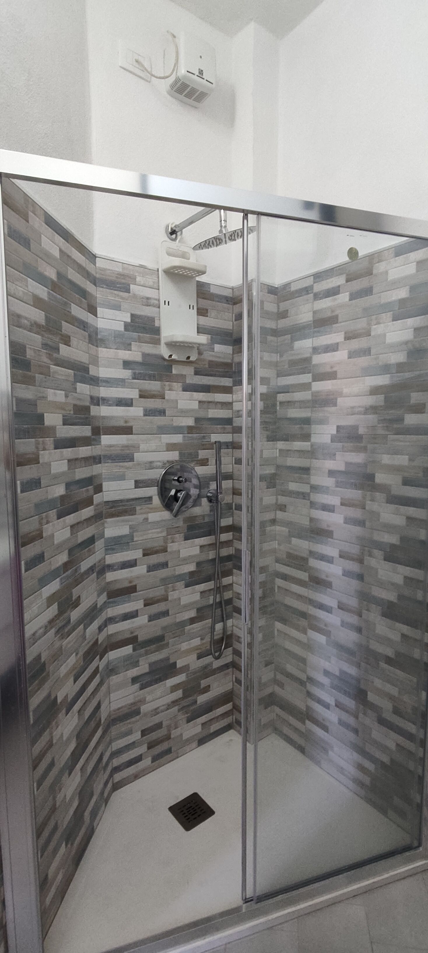 Une douche fermée par des parois en verre, avec un mur carrelé et un panneau de commande.