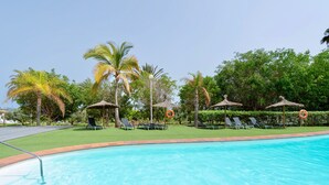Ein Swimmingpool mit Liegestühlen und Sonnenschirmen, umgeben von Palmen und viel Grün.