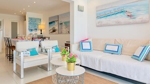 Ein modernes Wohnzimmer mit einer Couch, Sesseln, einem Esstisch und einem Gemälde eines Piers.