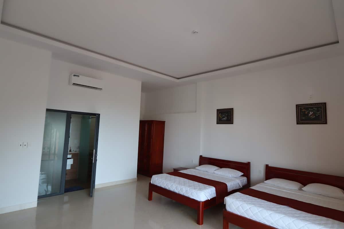 A hotel room with two single beds, a wooden wardrobe, a desk, and a glass door leading to a bathroom.