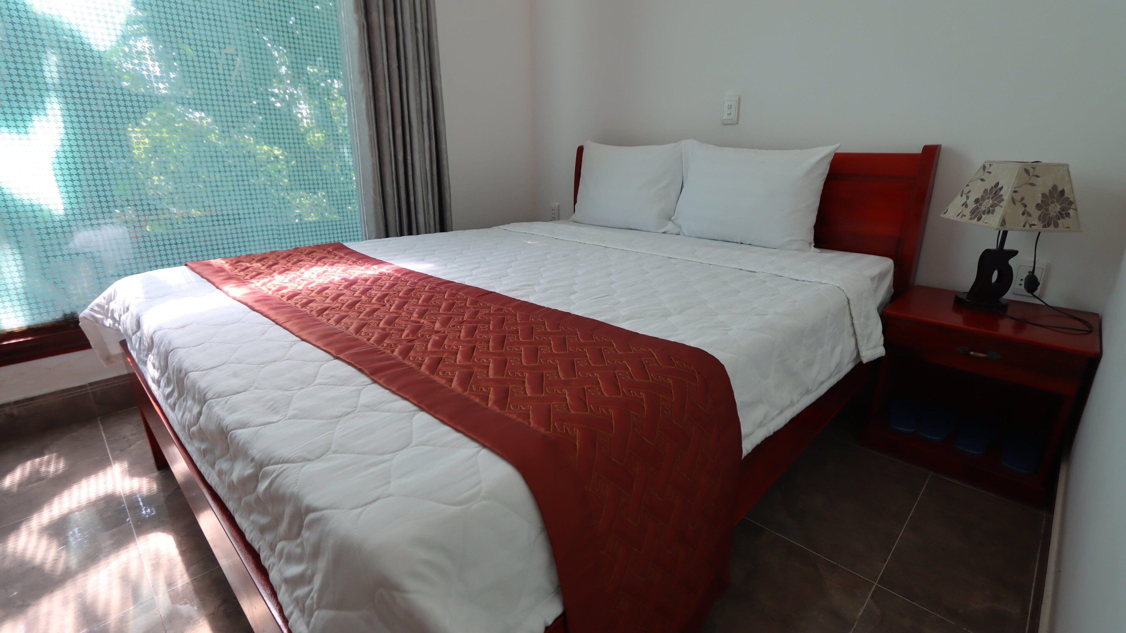 Een hotelkamer met een bed, nachtkastje, lamp en een raam met gordijnen.