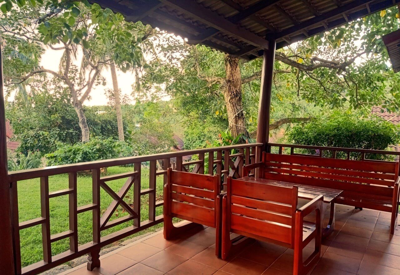 Un conjunto de banco y mesa de madera en un porche cubierto, con vistas a un jardín exuberante.