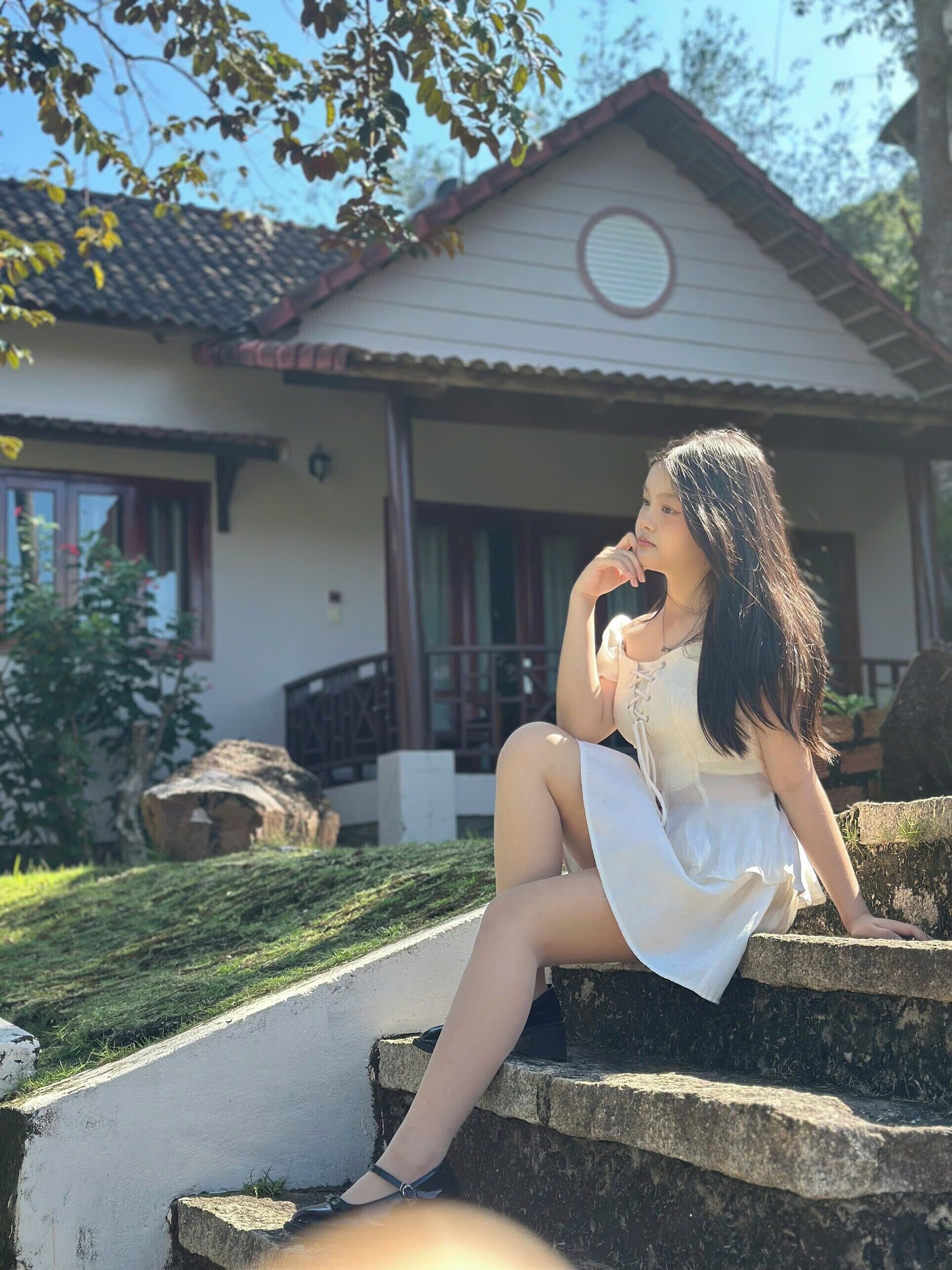 Uma pessoa sentada em degraus de pedra em frente a uma casa com telhado ladrilhado e uma janela circular.