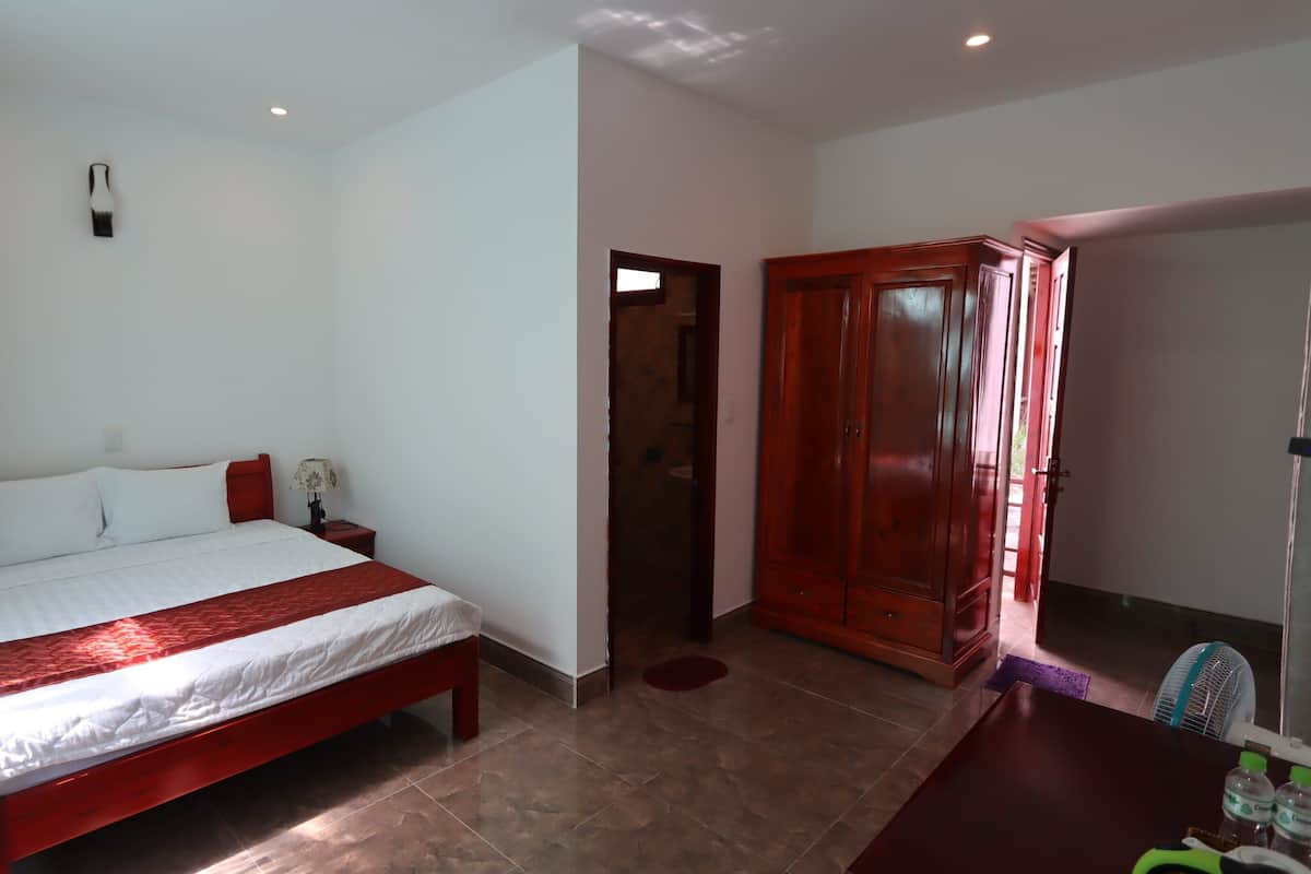 A hotel room with a bed, bedside table, lamp, wardrobe, and a view of the outside.