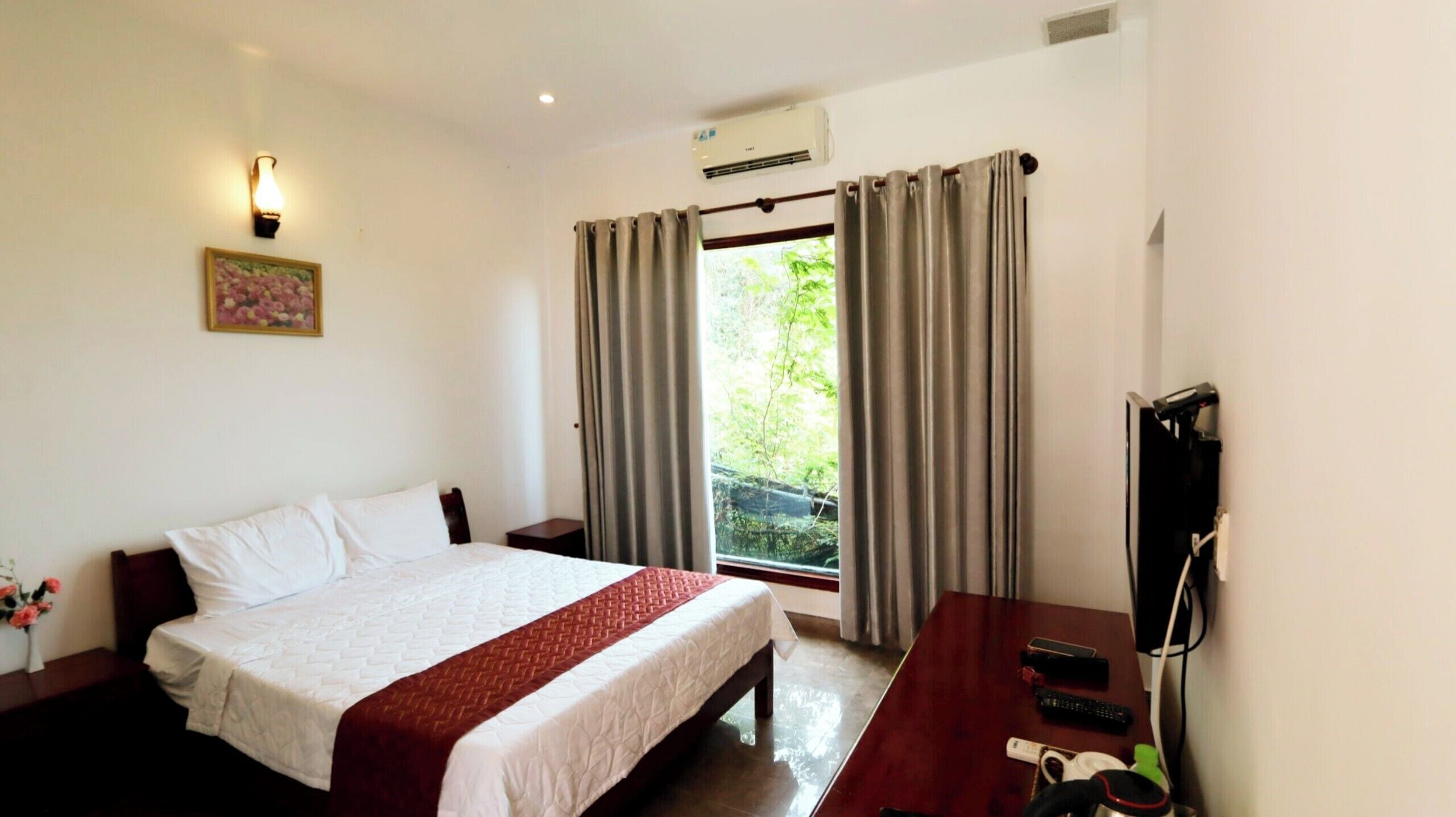 A hotel room with a bed, a desk with a TV, and a window with curtains.