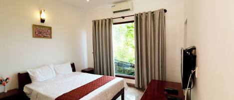 A hotel room with a bed, a desk with a TV, and a window with curtains.