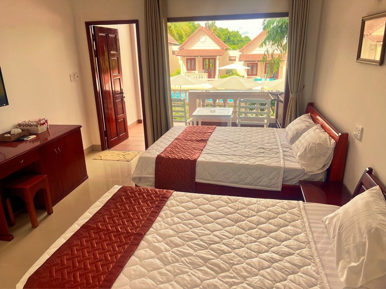 A hotel room with two beds, a desk, and a view of a pool and buildings.