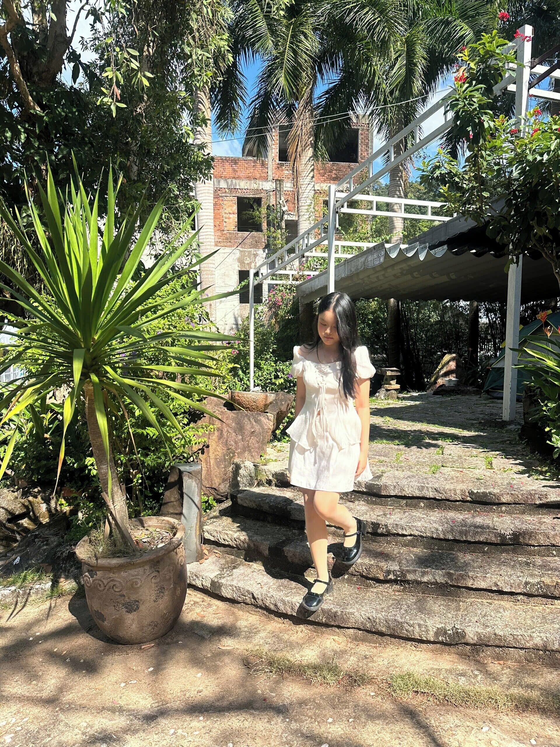 A person walking on stone steps surrounded by greenery and a building with a white structure.