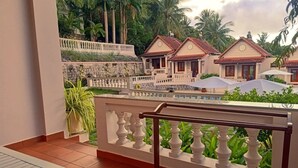A balcony with a white balustrade overlooking a pool area with umbrellas, surrounded by palm trees and a row of traditional-style buildings with red-tiled roofs. - Hong Bin Bungalow Resort (Phu Quoc)