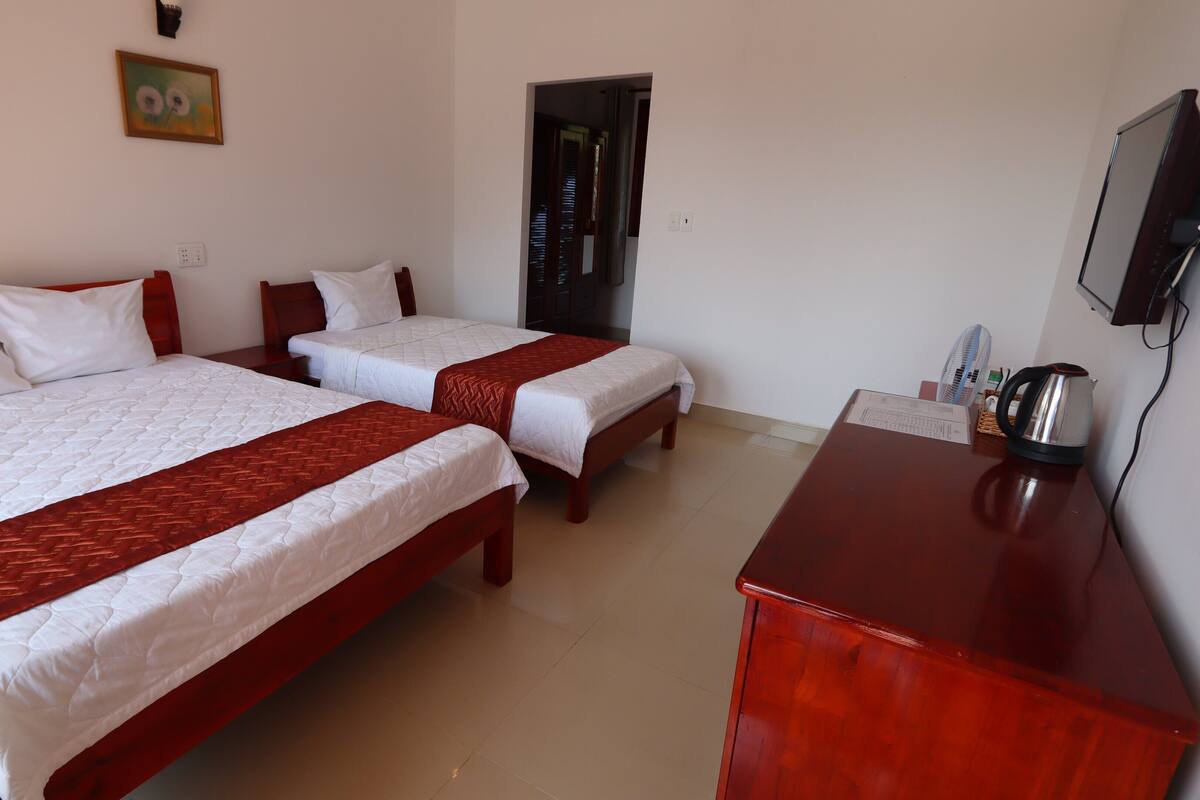 A hotel room with two beds, a desk, a kettle, and a television.
