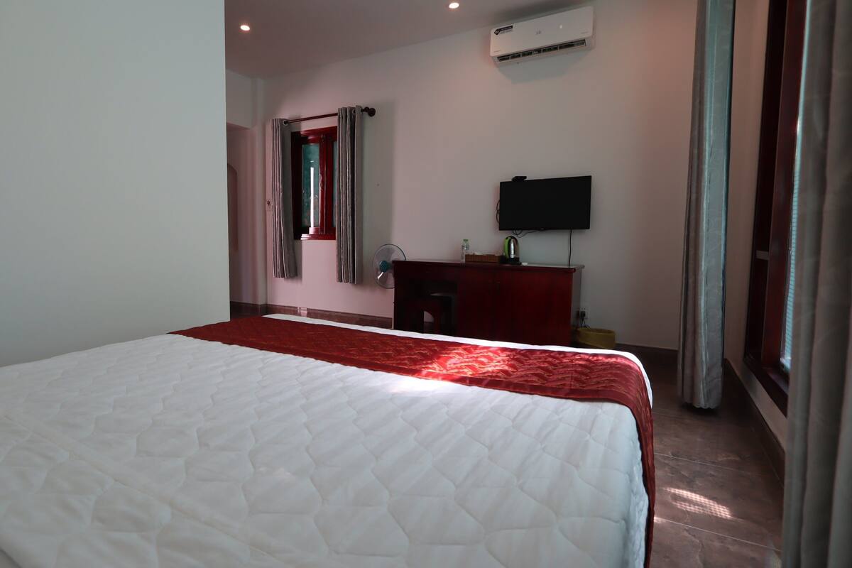 A hotel room with a large bed, a TV, a desk, and a window with curtains.