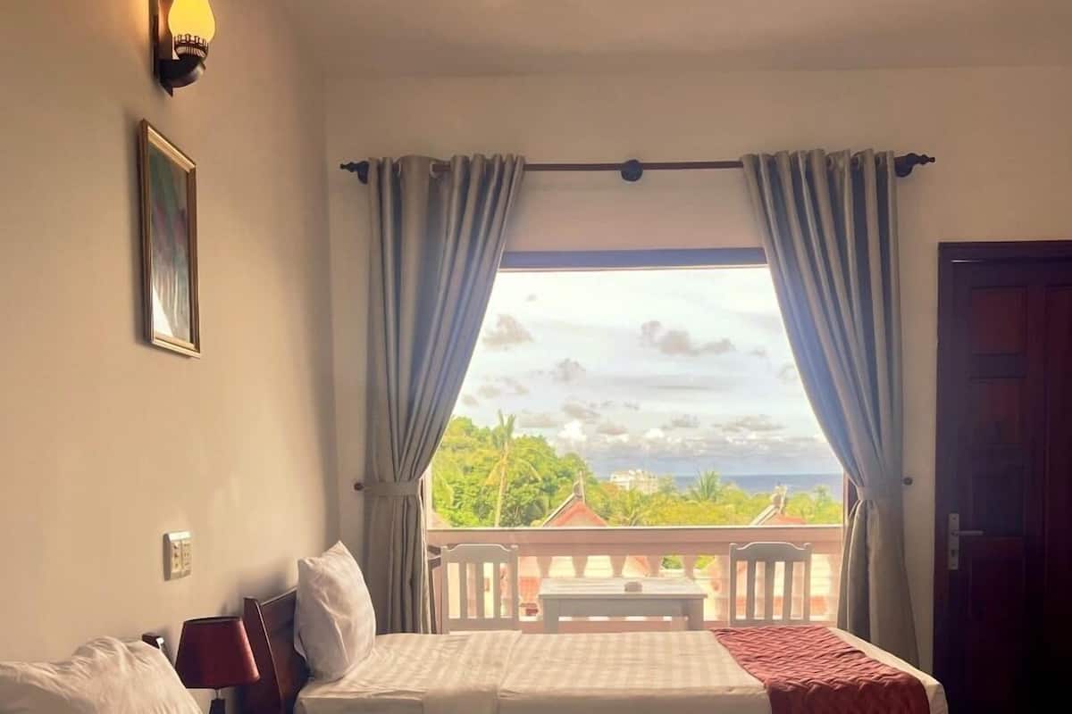A hotel room with two beds, a view of the outdoors, and a balcony with a table and chairs.