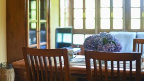 A dining area with a table set for two, a vase of flowers, and a view of a bay window with multiple panes. - Apartamento A (Picones)