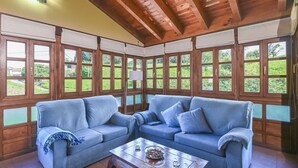 A room with two blue sofas, a wooden coffee table, and large windows with a view of greenery. - Apartamento A (Picones)