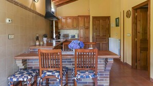 A kitchen with wooden cabinets, a central island with chairs, a microwave, and a sink. - Apartamento A (Picones)