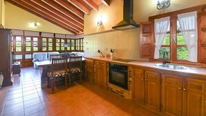 A kitchen with wooden cabinets, a stove, and a dining area with chairs and a table. - Apartamento A (Picones)