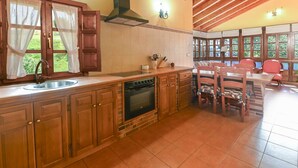 A kitchen with wooden cabinets, a sink, and a stove. There is a dining area with chairs and a table. - Apartamento B (Picones)