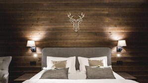 A bedroom with a wooden headboard, two bedside lamps, and a deer head decoration. - ARIETES MARMONT RESORT (Štrba)