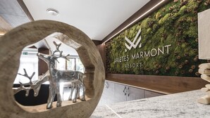 A reception area with a wooden reception desk, a wall-mounted sign for Arietes Marmont Resort, and a decorative wall with pinecones and greenery. - ARIETES MARMONT RESORT (Štrba)