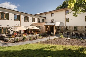 A hotel courtyard with outdoor seating, a stone pathway, and a sign for 'Royal Crown Cola'. - ARIETES MARMONT RESORT (Štrba)