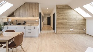 A modern kitchen with wooden cabinets, a dining area with a table and chairs, and a lofted sleeping area with a wooden slat wall. - ARIETES MARMONT RESORT (Štrba)
