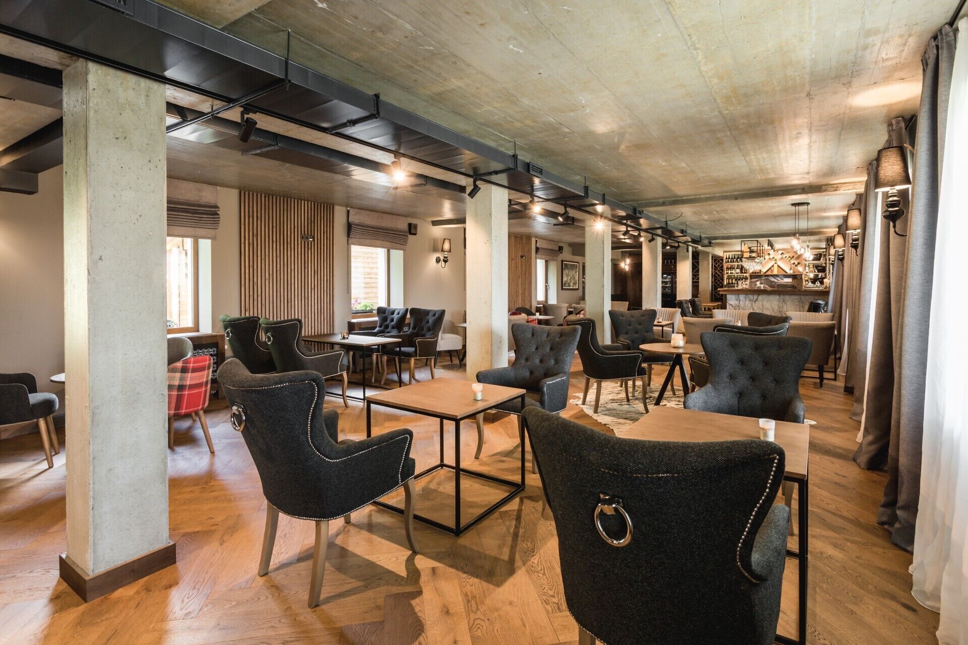 A spacious indoor area with multiple seating arrangements, including tables and chairs, and a bar area in the background.