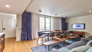 A modern living room with a sofa, a dining table with chairs, a TV, and a window with curtains. - Elegant Haussmannian Retreat in the Heart of Paris (Paris)