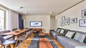 A modern living room with a sofa, dining table, chairs, and a TV screen. - Elegant Haussmannian Retreat in the Heart of Paris (Paris)