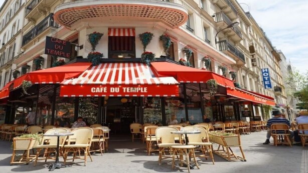 A café with a red and white striped awning, outdoor seating with wicker chairs and tables, and a sign reading "CAFÉ DU TEMPLE". - Elegant Haussmannian Retreat in the Heart of Paris (Paris)
