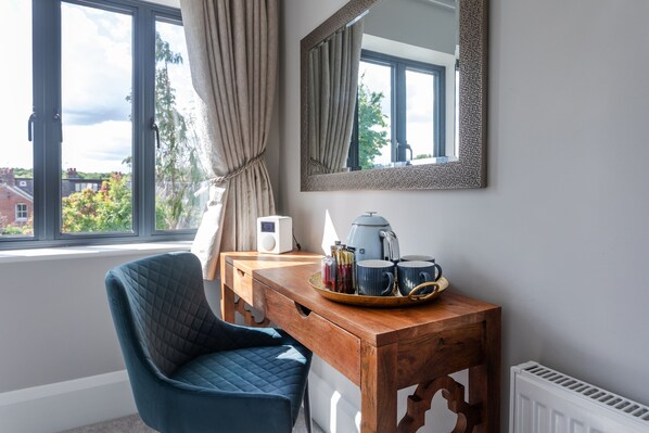 A room with a wooden table, a blue chair, a mirror, a window with curtains, and a radiator.