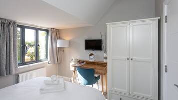 A bedroom with a bed, a desk with a chair, a wardrobe, and a television on the wall.