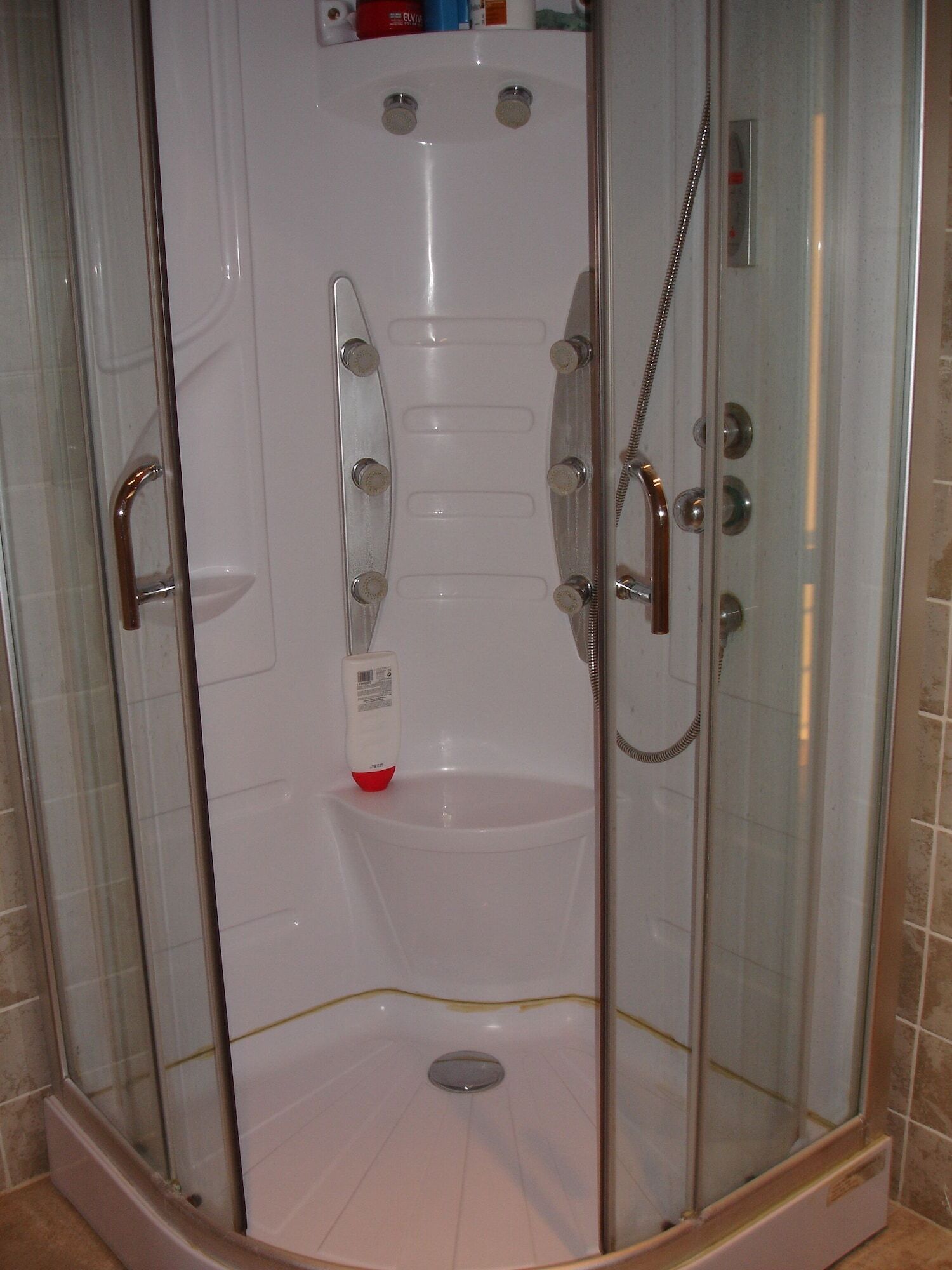 A glass-enclosed shower stall with a handheld showerhead, a handheld shower head, and a bottle of shampoo.