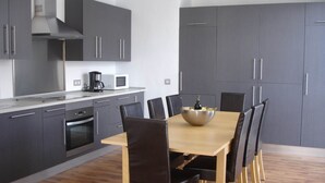 A modern kitchen with grey cabinets, a stainless steel range hood, and a dining area with a wooden table and black chairs. - PICAFORT2, PRIVATE POOL, free wifi, beach, air conditioning, barbecue (IB)