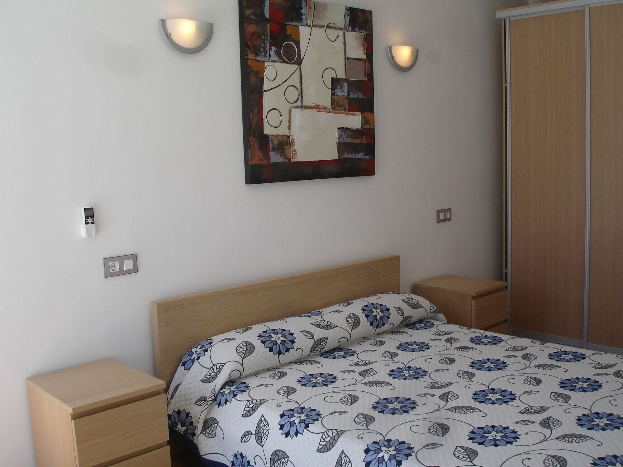 A bedroom with a wooden bed, two bedside tables, a wall-mounted abstract painting, and a wardrobe.