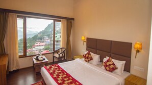 Una habitación de hotel con una cama grande, dos lámparas de noche, una silla, una mesita y una ventana con cortinas.