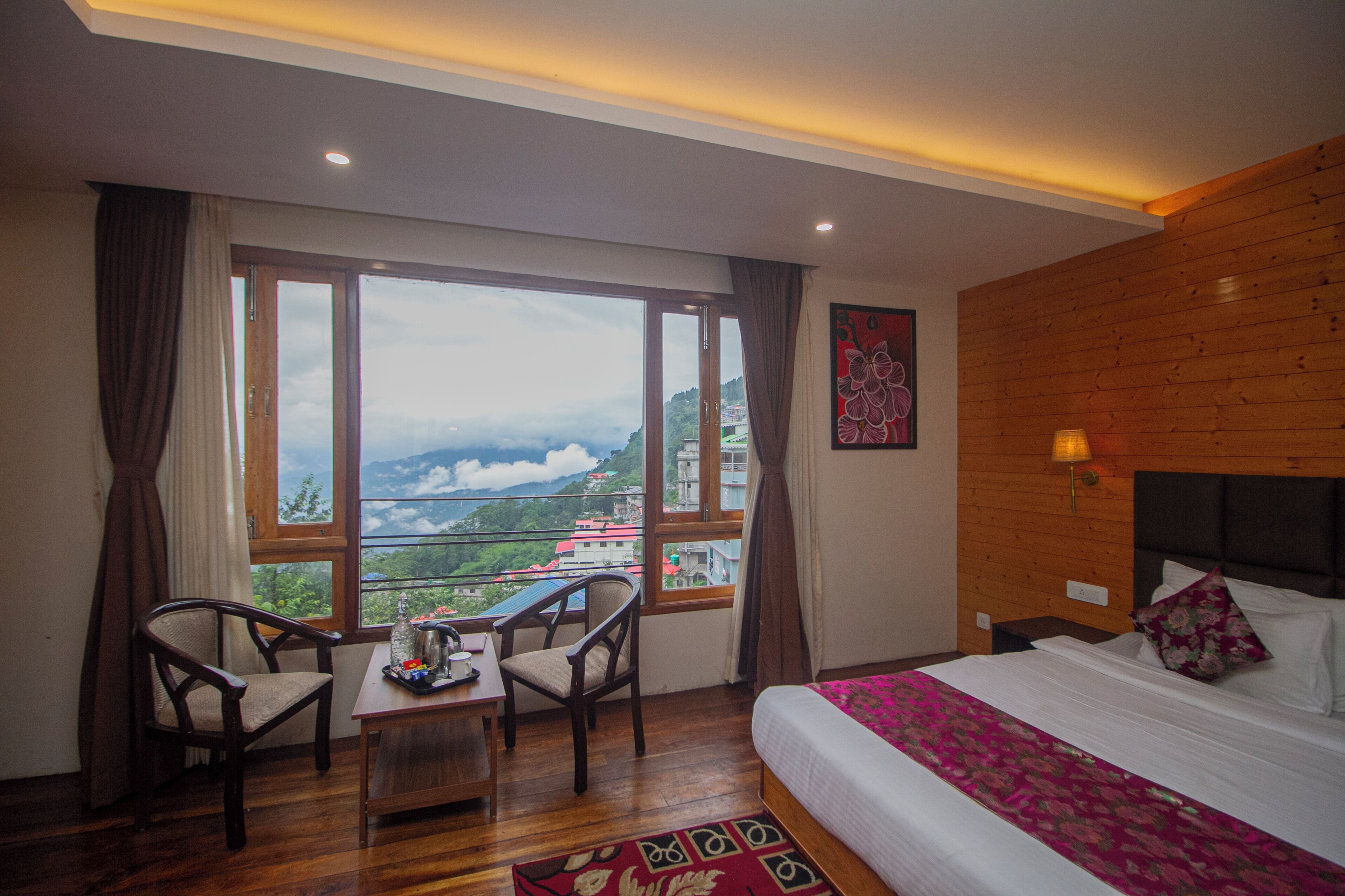 A hotel room with a large window offering a mountain view, a wooden headboard, and a bed with a floral bedspread.
