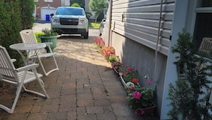 A paved patio with outdoor furniture, a vehicle parked in the driveway, and a row of potted plants with flowers.
