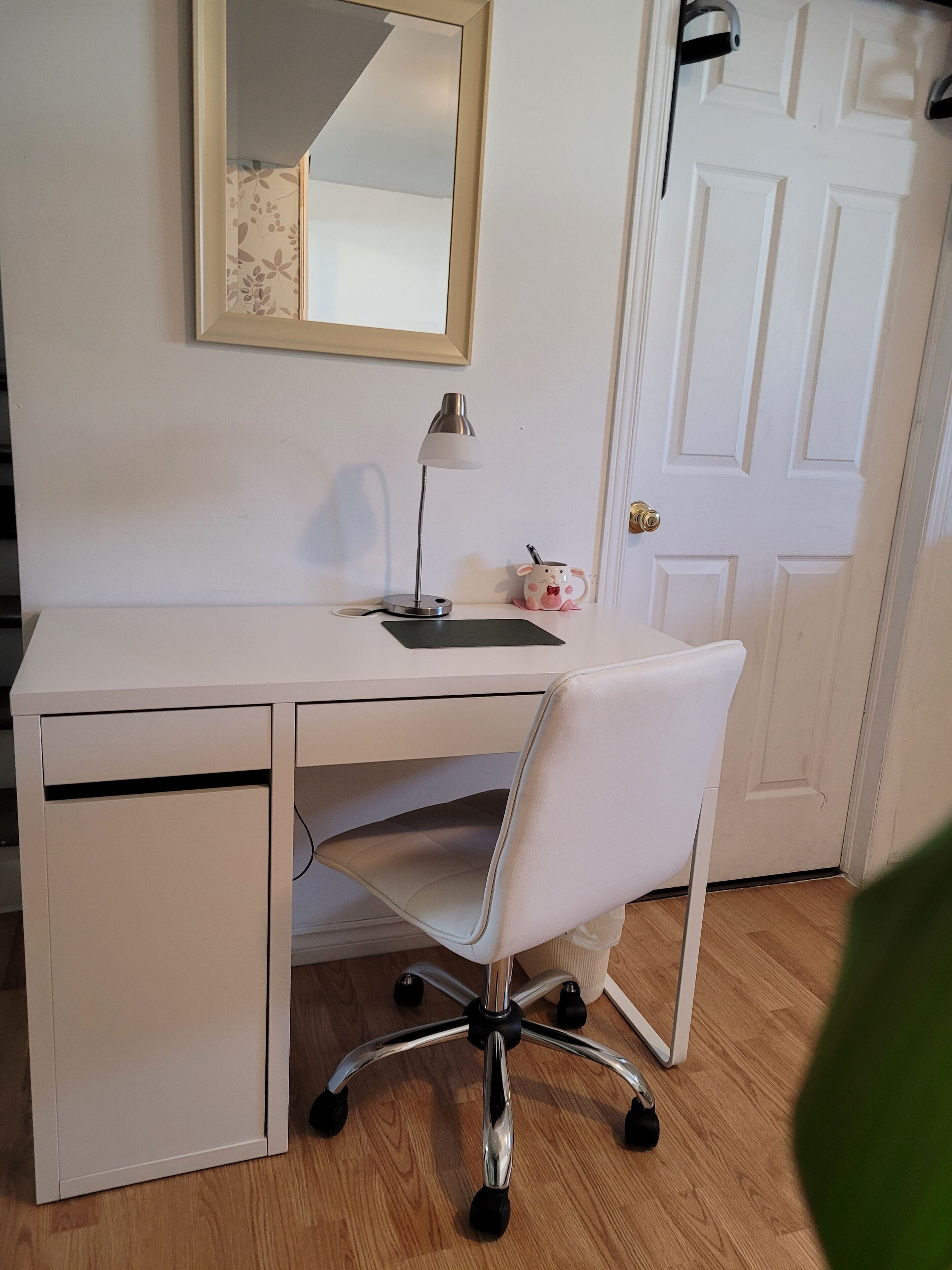 Een wit bureau met een stoel, een lamp en een klein roze spaarvarken op het bureau.