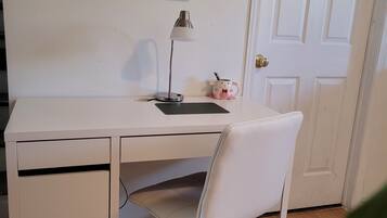 Een wit bureau met een stoel, een lamp en een klein roze spaarvarken op het bureau.