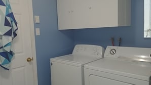 A laundry room with two white washers and dryers, a blue wall, and a white door with a geometric-patterned curtain.