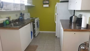 A compact kitchen with white cabinets, a gas stove, a refrigerator, and a small countertop.
